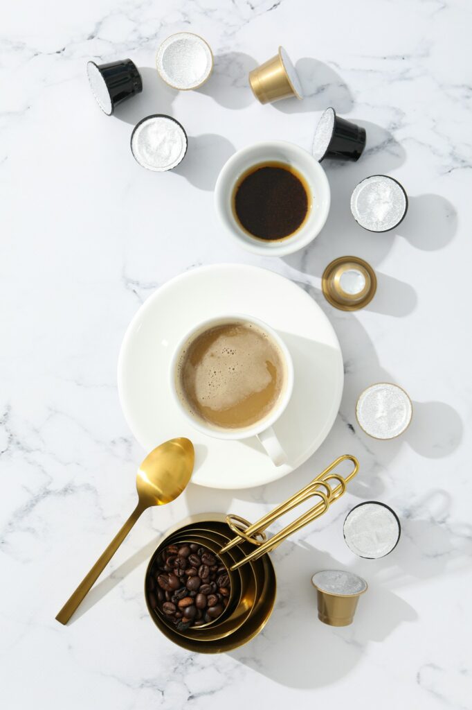 Coffee capsules and beans, cups with coffee drink on marble background, top view