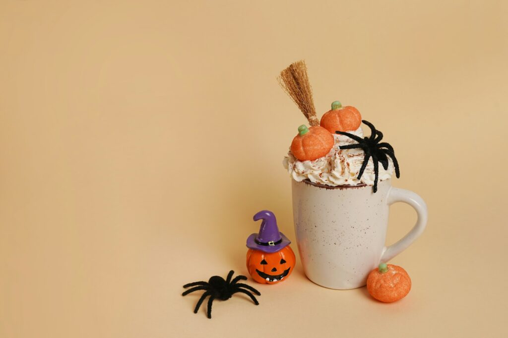 Halloween theme with a cup of coffee, decor pumpkins, spider and witch's broom, yellow background