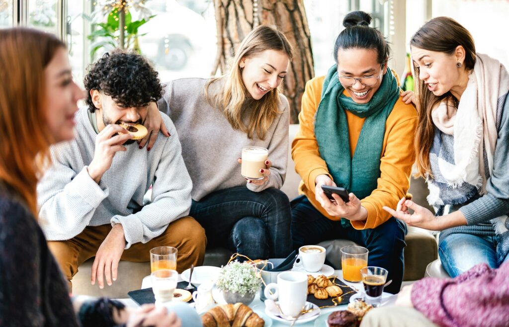 Multicultural friends playing with mobile phone at coffee bar