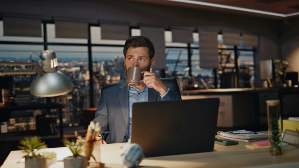 Overworked man sipping coffee at night room closeup. Businessman looking laptop